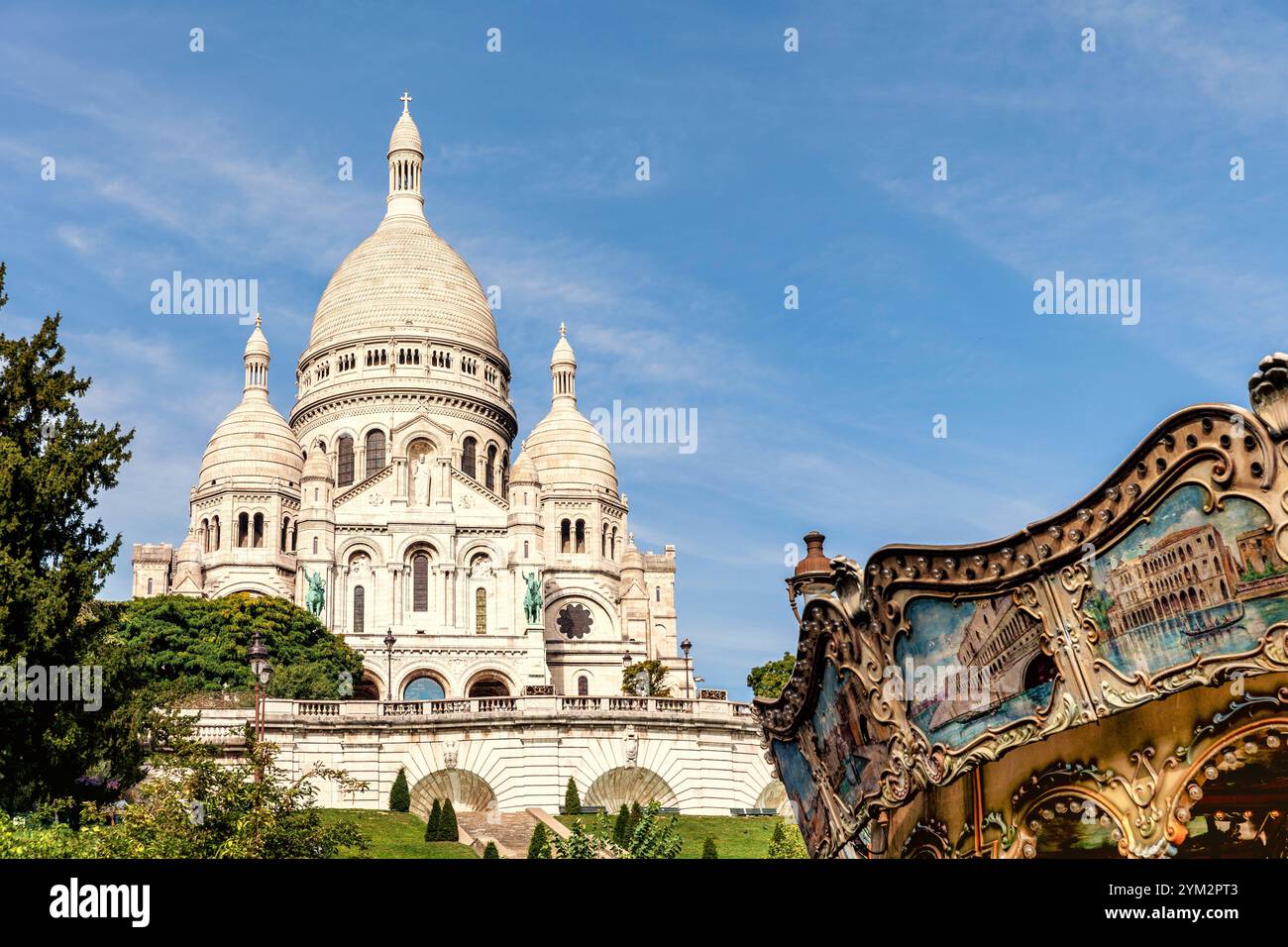 Ein idyllisches Bild der Basilika SacrÃ -coeur auf dem Montmartre à Paris, Frankreich. Die weiße Fassade der berühmten Kirche strahlt im Sonnenlicht, während im Vordergrund ein nostalgisches Karussell mit bemalten Paneelen zu sehen ist, das der Szene einen charmanten Vintage-Touch verleiht. Umgeben von Grünflächen und unter einem klaren blauen Himmel fängt dieses Foto die malerische Atmosphäre von Montmartre ein. *** Une image idyllique de la basilique du Sacré coeur sur Montmartre à Paris, France la façade blanche de la célèbre église brille au soleil, tandis qu'un carrousel nostalgique avec un p peint Banque D'Images