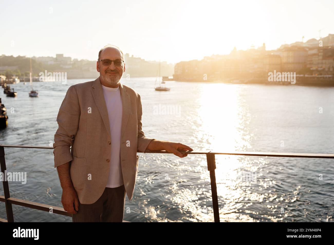 Homme en veste légère profitant du coucher du soleil sur le front de mer dans un port animé Banque D'Images
