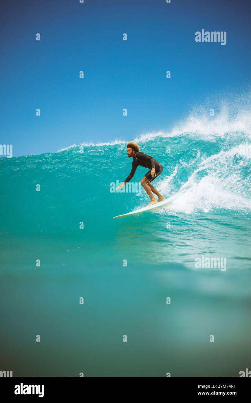 Un surfeur surfe sur une vague dans l'océan. Le surfeur porte une combinaison noire. L'océan est calme Banque D'Images