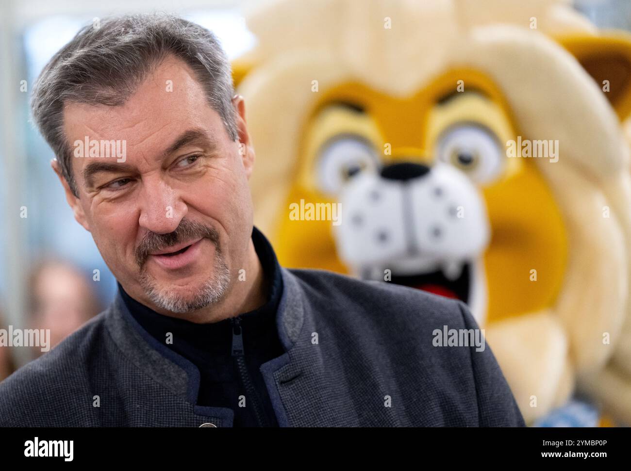 Munich, Allemagne. 21 novembre 2024. Markus Söder (CSU), ministre-président de Bavière, visite l'école primaire de Infanteriestraße et présente la nouvelle licence cycliste. Derrière Söder se trouve la mascotte du gouvernement bavarois. Il accompagne les élèves tout au long de leurs années de scolarité primaire. L'objectif est que les enfants puissent se déplacer en toute sécurité dans la circulation, reconnaître les dangers et éviter les accidents autant que possible. Crédit : Sven Hoppe/dpa/Alamy Live News Banque D'Images