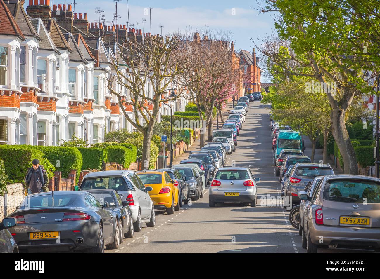 Londres, Royaume-Uni - 10 avril 2024 - Une voiture traversant une rue londonienne bordée de maisons mitoyennes et de voitures garées dans le quartier de Crouch End Banque D'Images