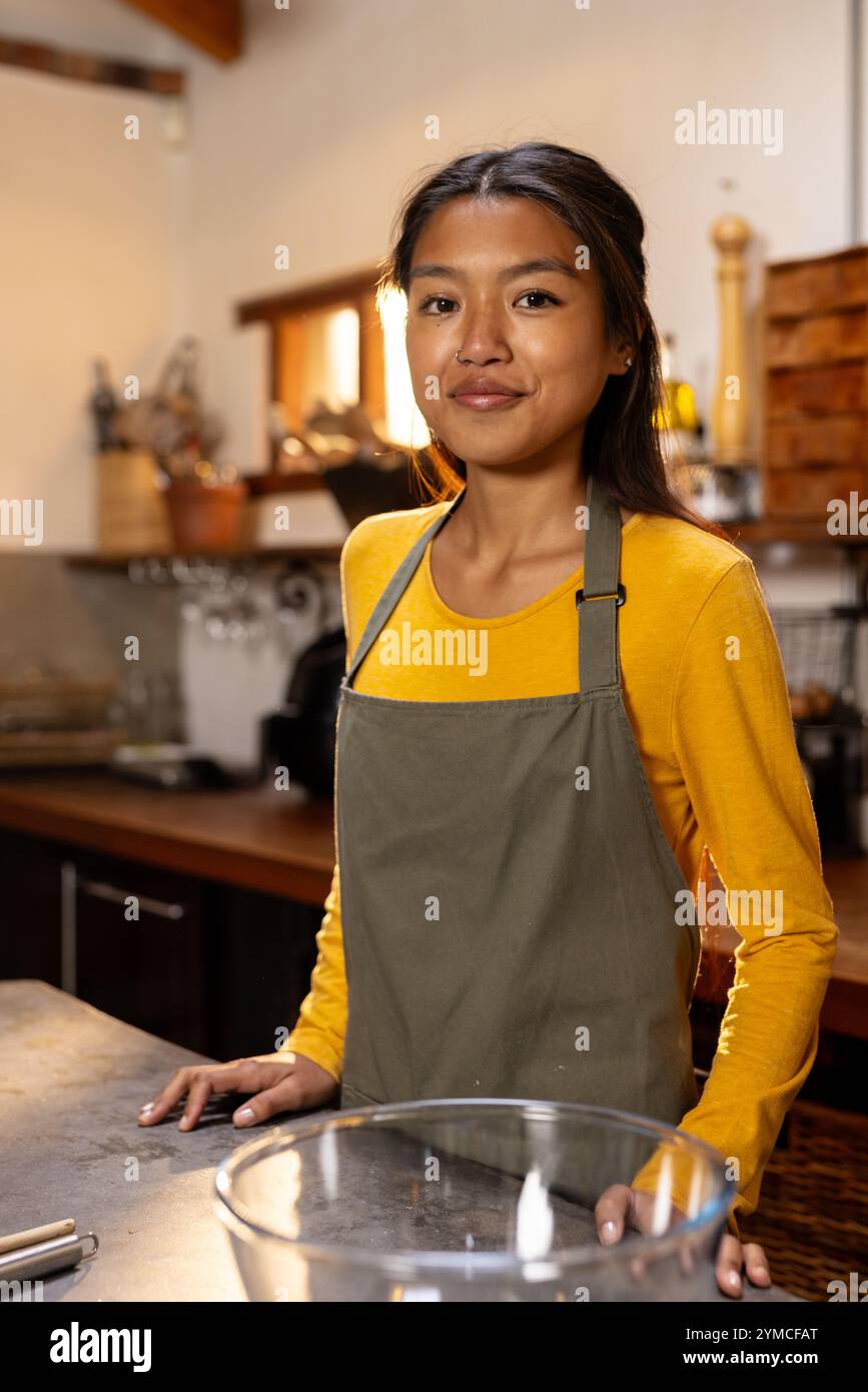 Adolescente asiatique dans la cuisine portant un tablier, se préparant à cuisiner à la maison. vacances, préparation, célébration, festive Banque D'Images