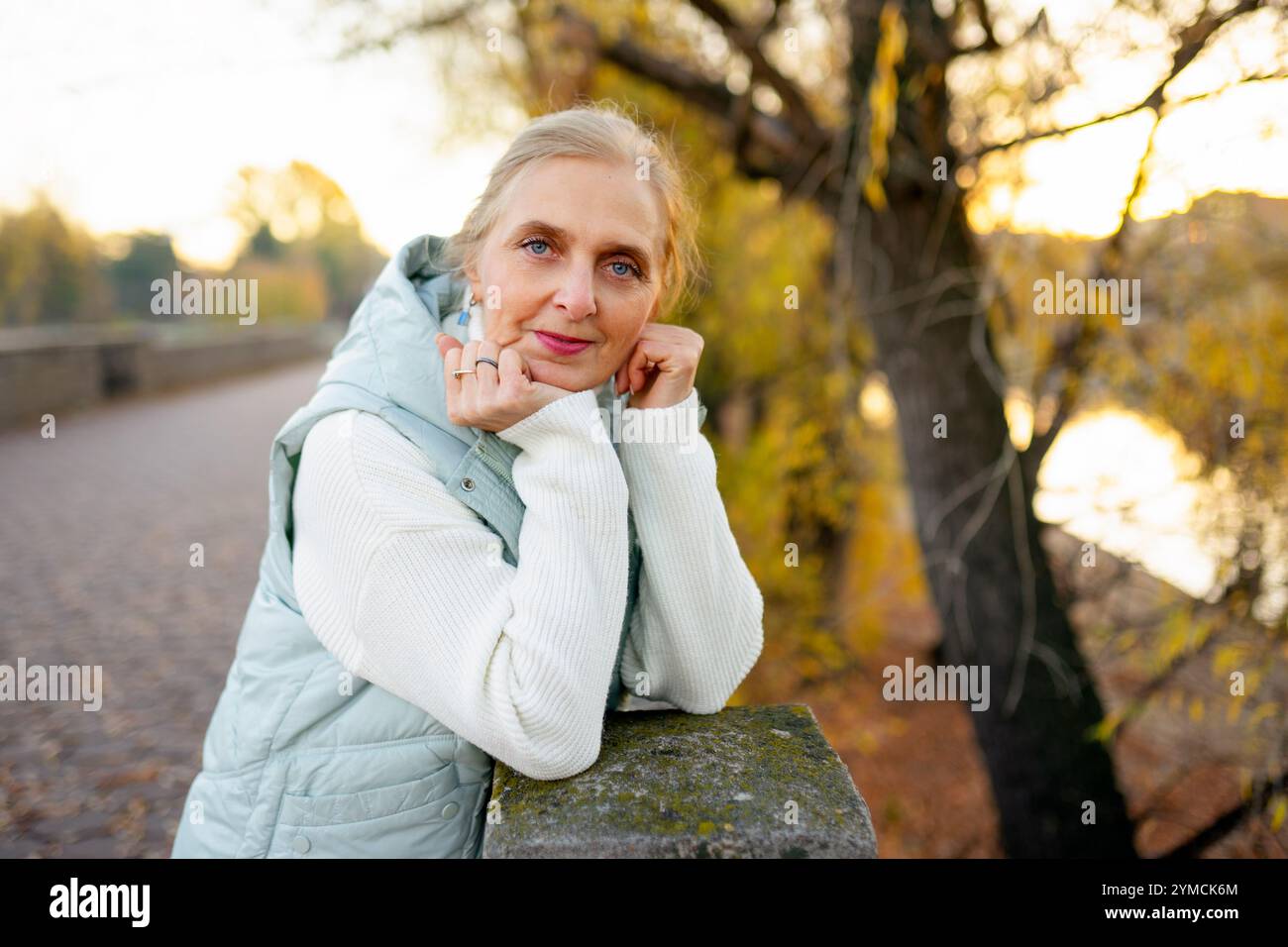 Portrait d'une femme appuyée sur un mur par la rivière en automne Banque D'Images