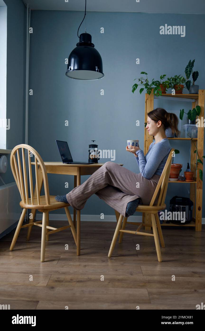 Femme tenant une tasse et regardant un ordinateur portable à la maison Banque D'Images