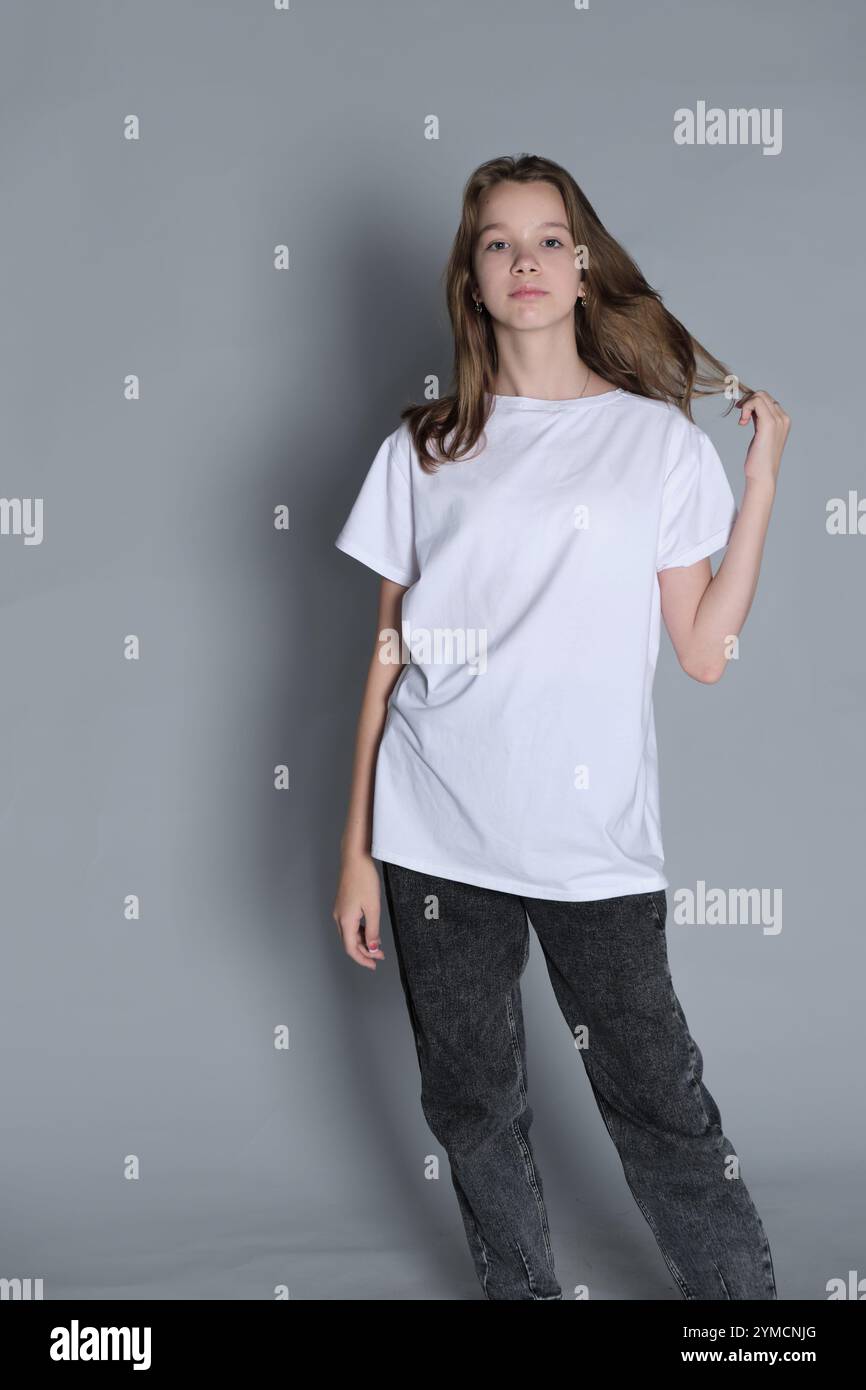 Une adolescente se tient debout dans un t-shirt blanc, regardant sur le côté avec un look pensif. Ce portrait souligne la curiosité et les reflets intérieurs communs Banque D'Images