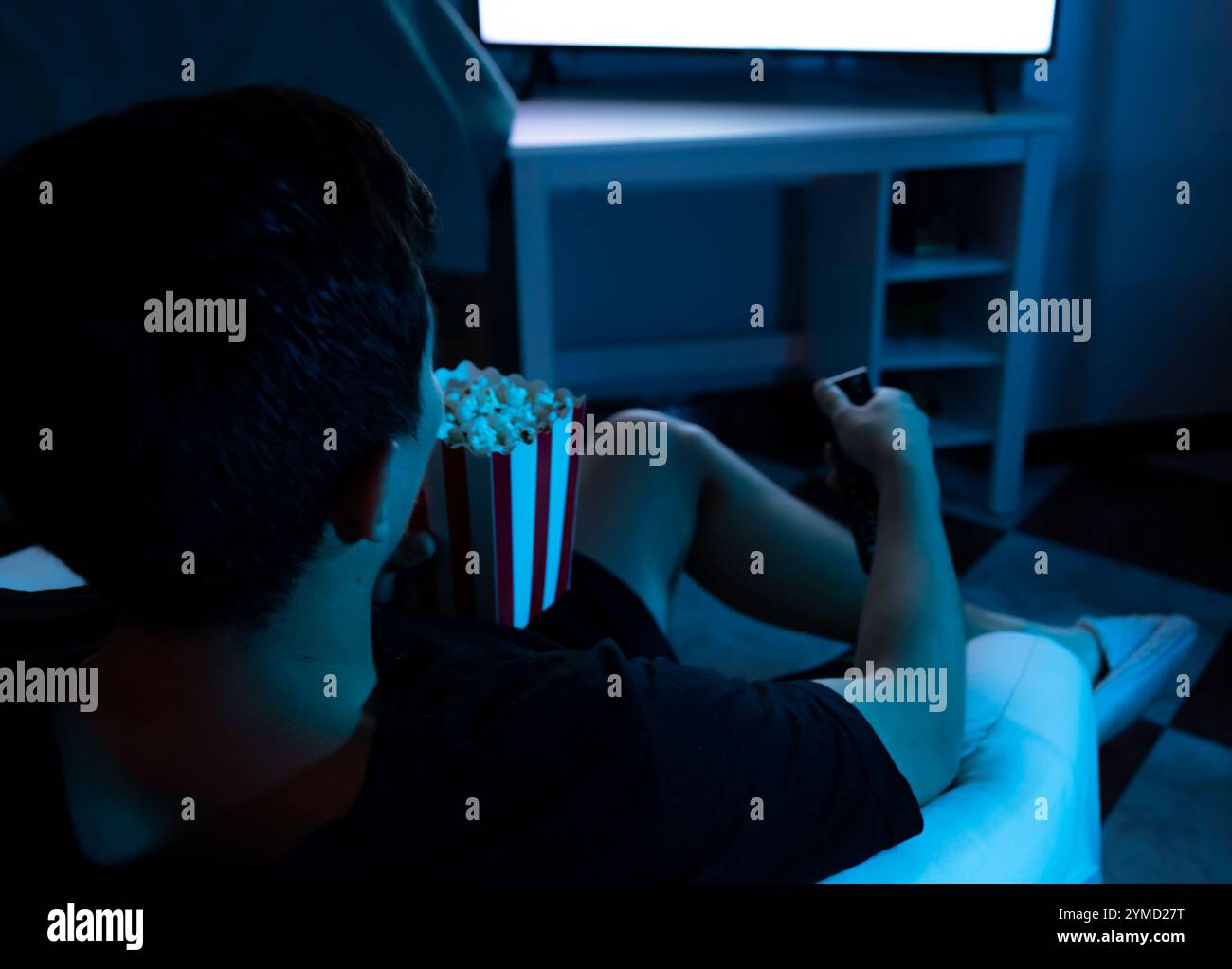 Vue de dessus d'un jeune homme regardant la télévision avec pop-corn mangeant dans le confort de sa maison Banque D'Images