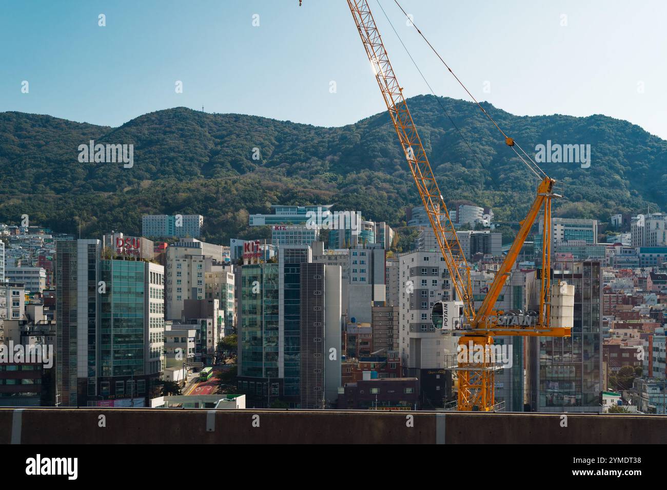 Ligne d'horizon urbaine moderne avec grue de construction sur un fond de montagne luxuriante en plein jour Banque D'Images