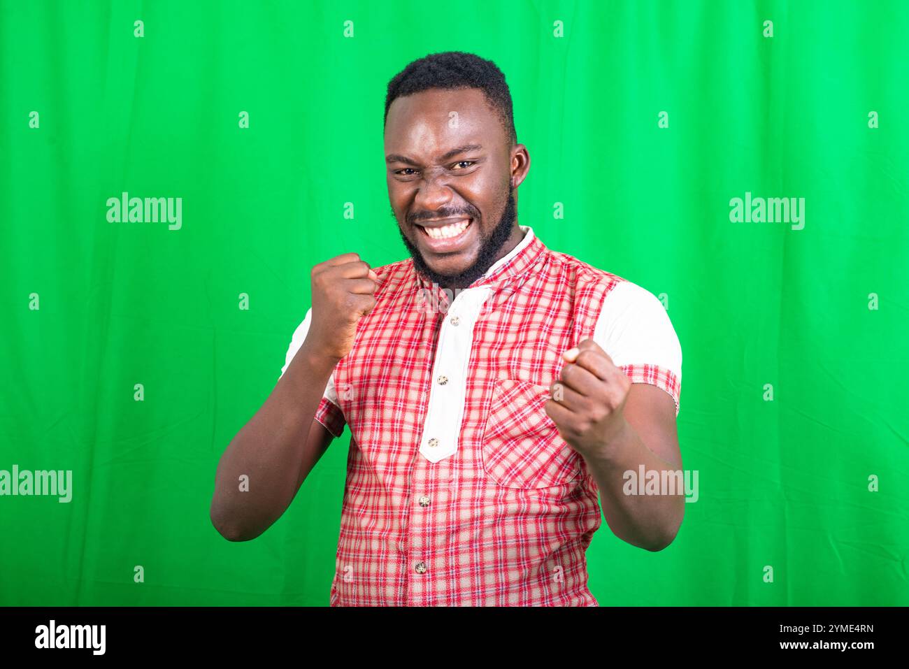 un beau jeune homme barbu en chemise debout sur fond vert montrant le geste gagnant en riant. Banque D'Images