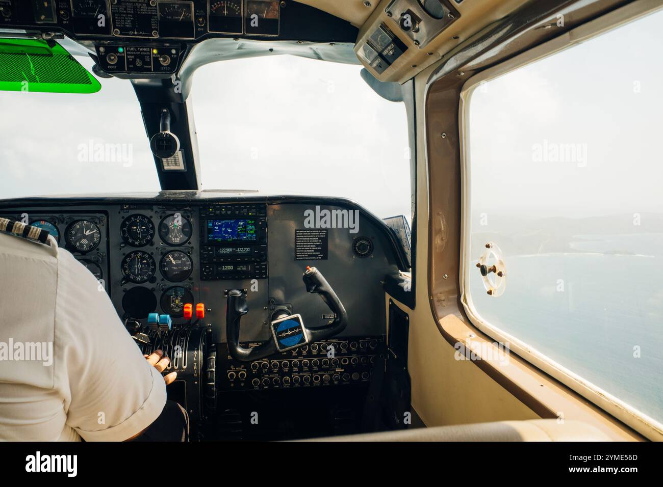 Gros plan d'un homme dans un cockpit pilotant un petit avion à quatre places, poussant des boutons sur le panneau de commande avec des collines et des prairies à distance. ph de haute qualité Banque D'Images