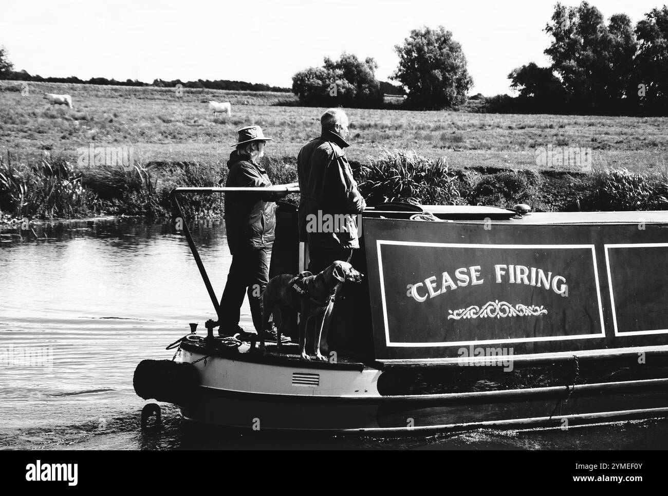 CAMBRIDGESHIRE, Royaume-Uni - 18 AOÛT 2017 : couple avec chien voyageant sur un bateau étroit traditionnel le long de la rivière Great Ouse. Photo historique noir et blanc. Banque D'Images