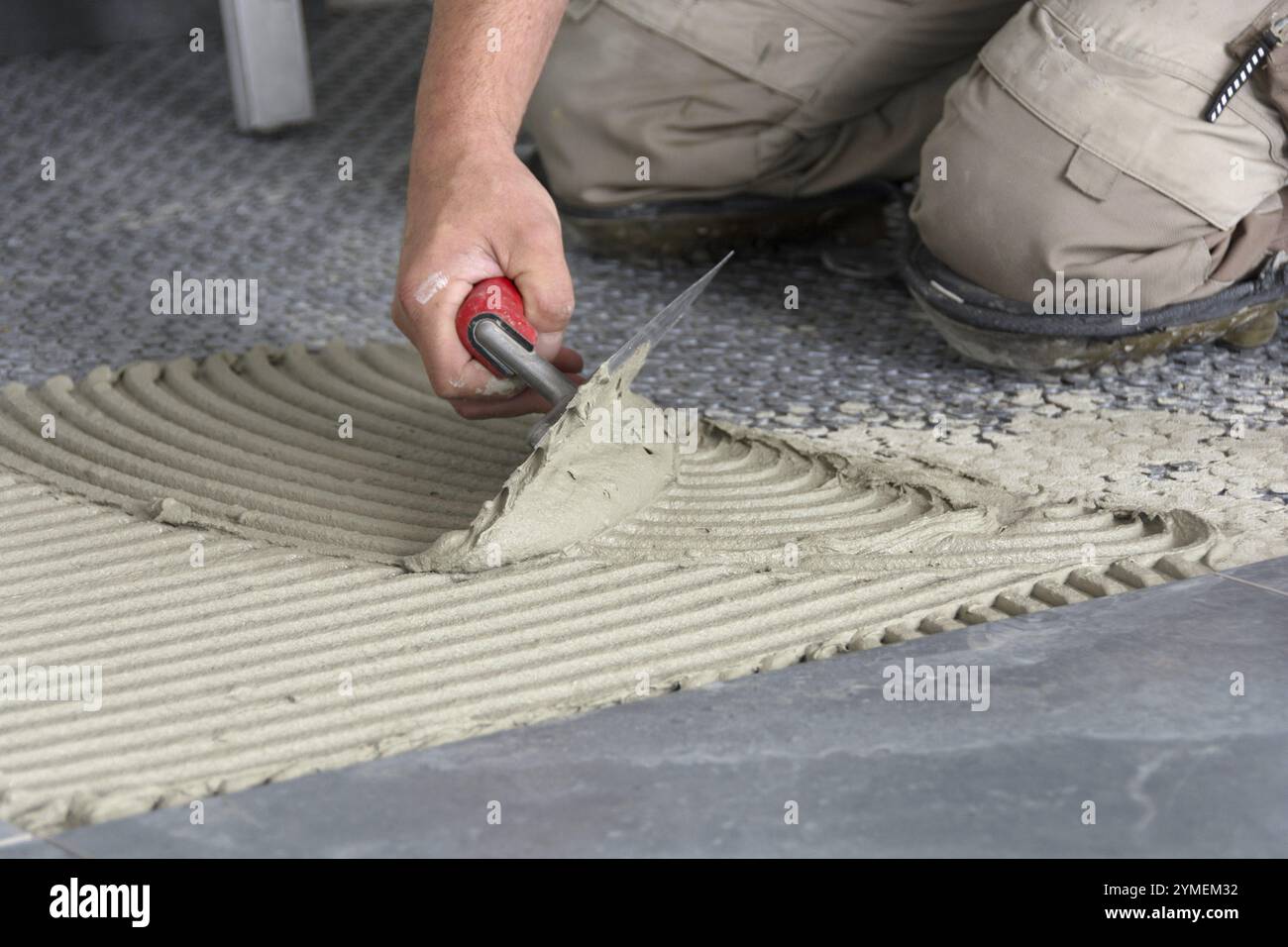 Gros plan à la main avec une truelle crantée lors de l'application de l'adhésif pour carreaux Banque D'Images