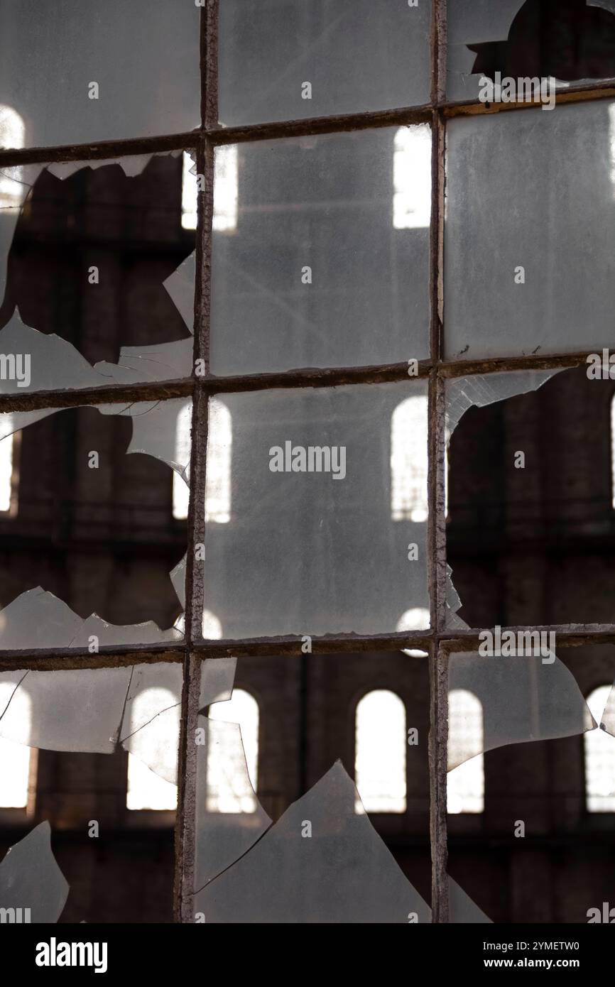 Gros plan de verre brisé dans une fenêtre d'un bâtiment industriel abandonné, sur fond urbain. Banque D'Images