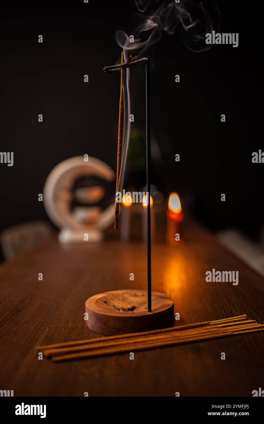 Un bâton d'encens brûlant et générant de la fumée aromatique entouré de petites bougies Banque D'Images