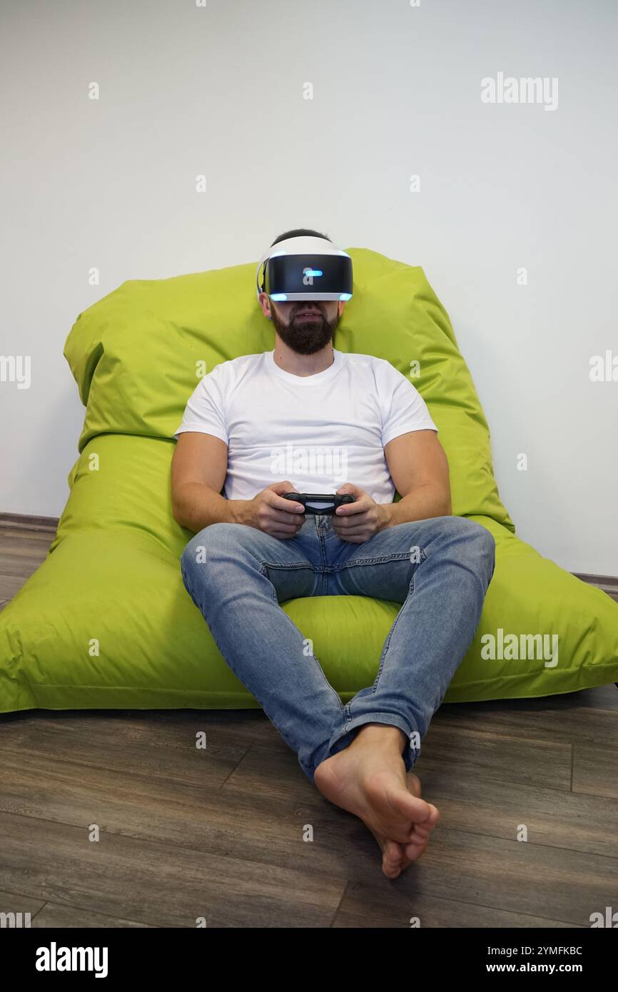 Homme portant casque VR, assis confortablement sur le sac de haricot vert tout en jouant avec contrôleur Banque D'Images