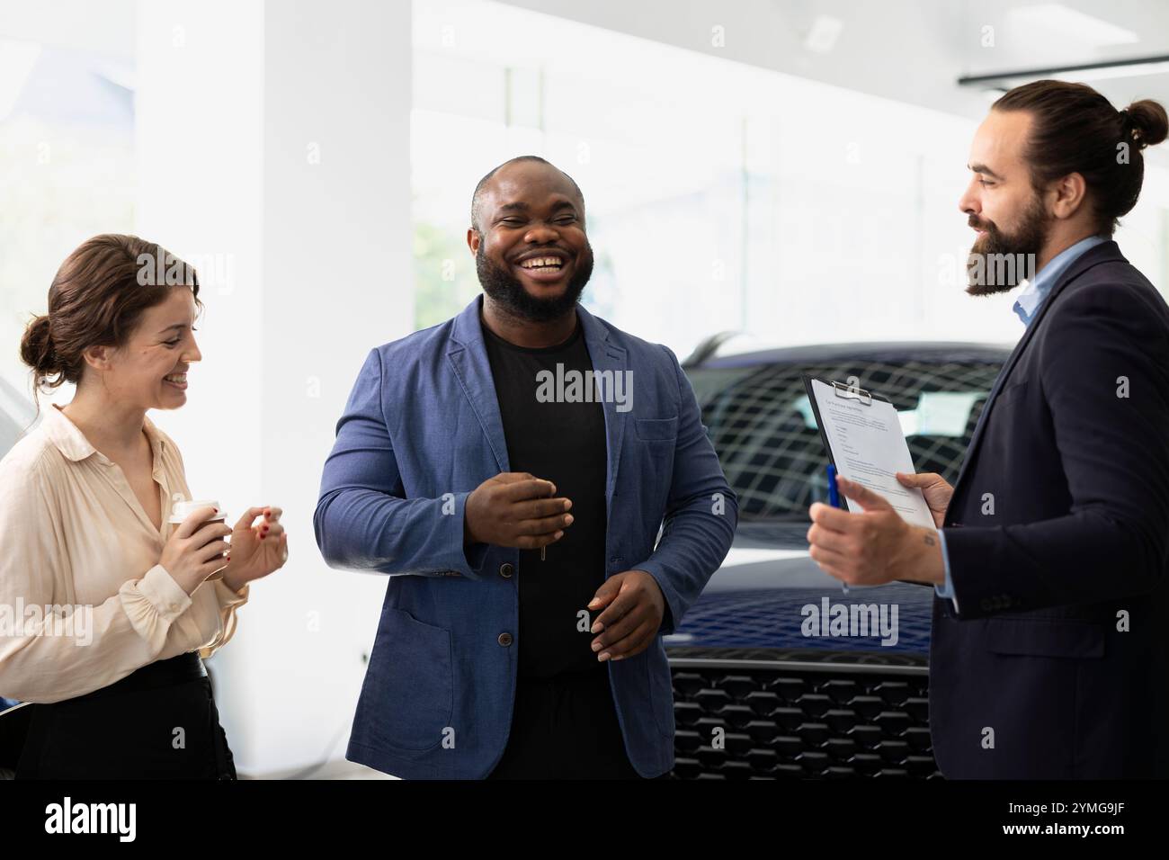 Vendeur de voiture drôle dans la concession faire rire les clients pour aider à solidifier l'affaire, gagner des bonus de commission sur chaque vente. Agent racontant des blagues aux clients pour les amuser, persuadant d'acheter un véhicule Banque D'Images