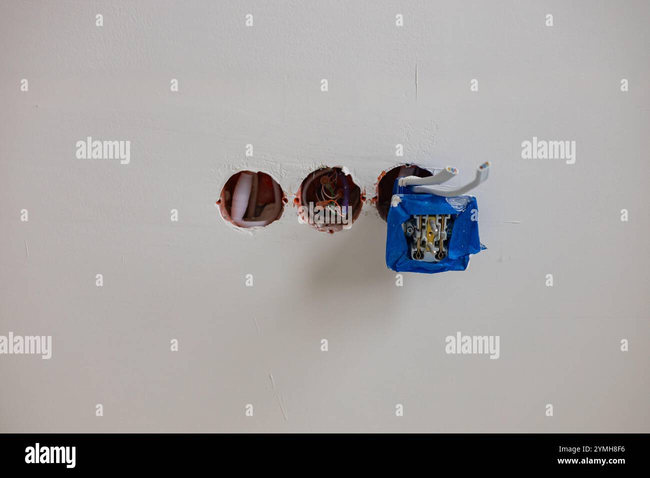 Installation de la prise électrique en cours avec les fils exposés et la boîte de jonction recouverte de ruban de protection sur le mur plâtré blanc. Banque D'Images