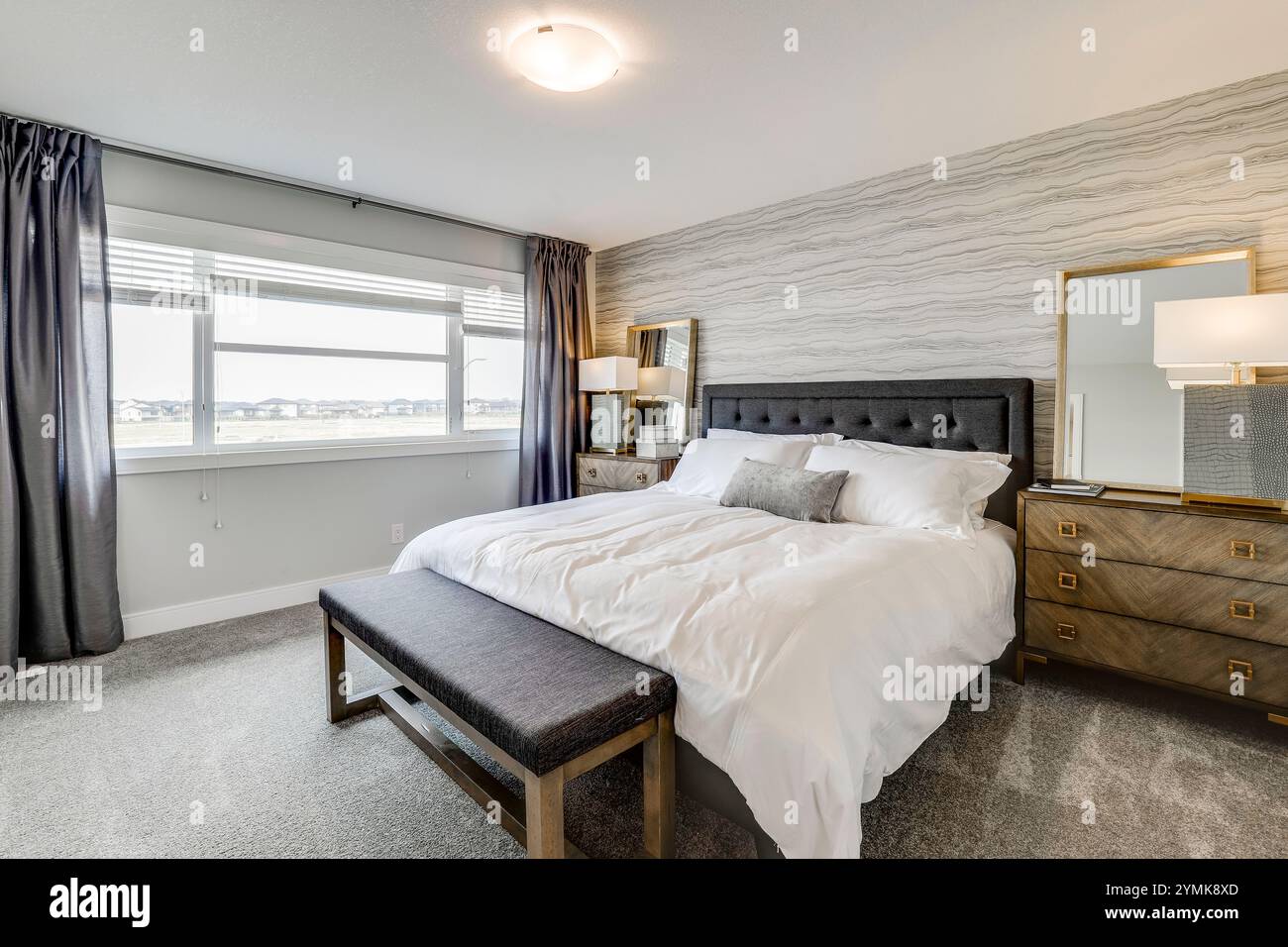 Une chambre avec un grand lit, une commode et un miroir. Le lit est recouvert de draps et oreillers blancs Banque D'Images