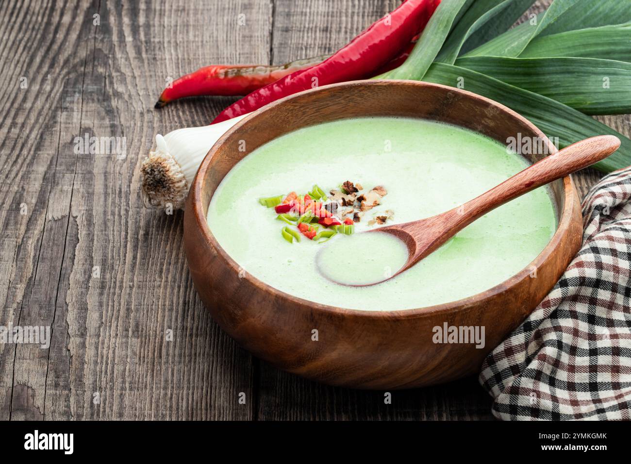 Soupe crémeuse de poireaux avec piment dans un bol en bois sur une table rustique Banque D'Images