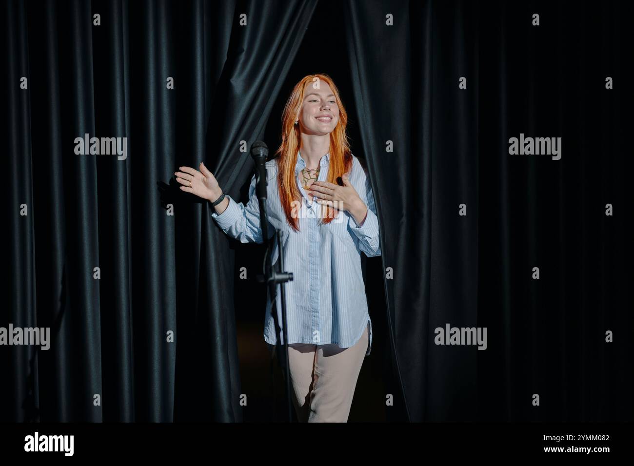 Femme souriante debout derrière les rideaux Black Stage Banque D'Images