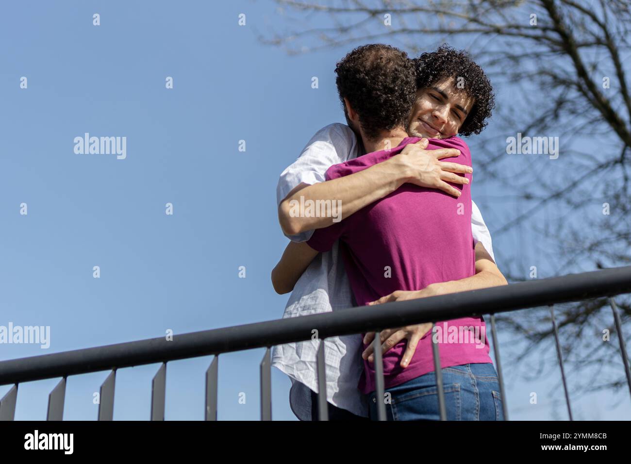 Couple gay brésilien embrassant tendrement à l'extérieur sur fond d'un ciel bleu clair. Copier l'espace Banque D'Images