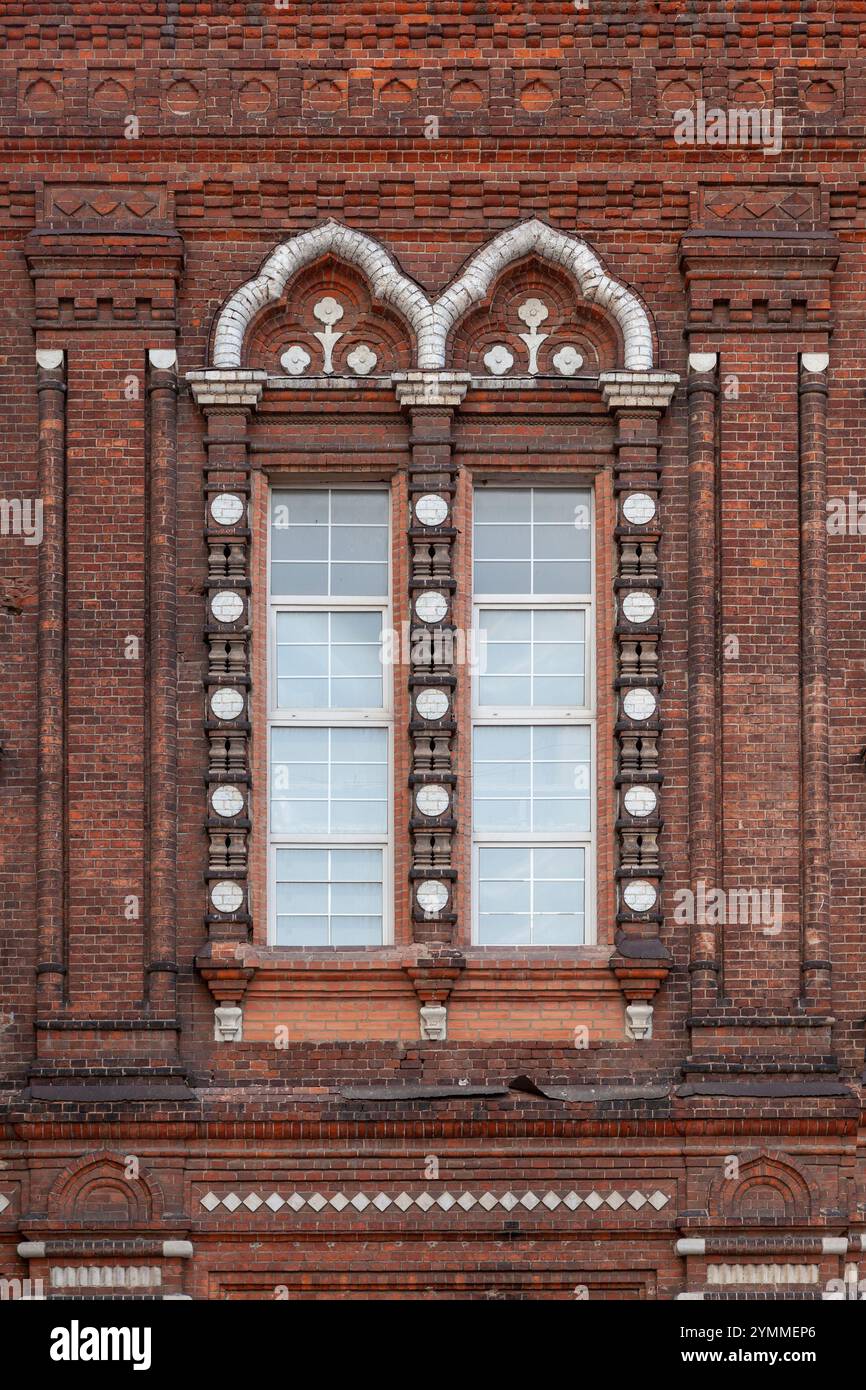 Fragment du mur d'un ancien bâtiment en briques avec une fenêtre encadrée d'un cadre à motifs. Banque D'Images