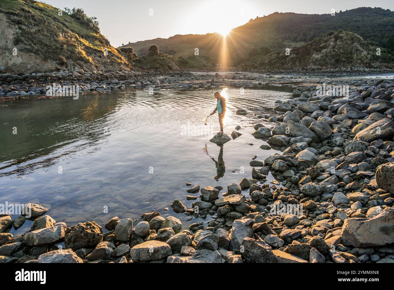 Adolescent avec filet debout sur la côte rocheuse au coucher du soleil Banque D'Images