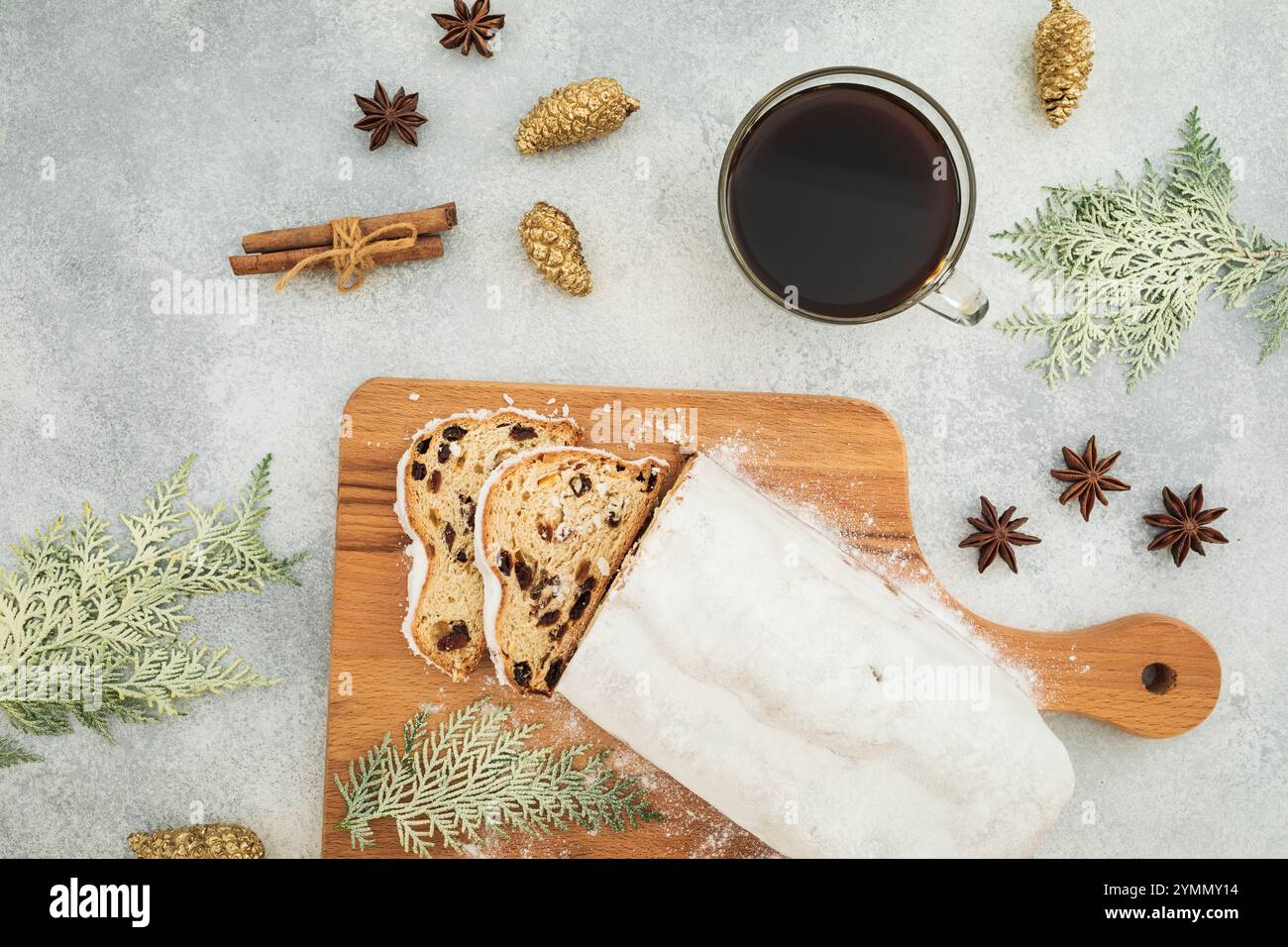 Nature morte festive avec gâteau stollen traditionnel de Noël sur une planche de bois, une tasse de café noir, des bâtons de cannelle, des étoiles d'anis, des pommes de pin dorées, un Banque D'Images
