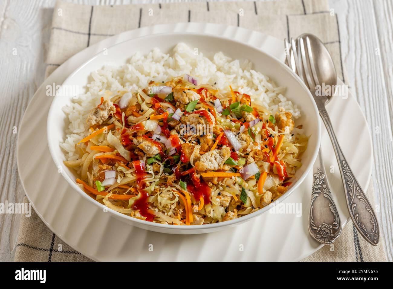 roulé aux œufs de tofu, chou sautés, tofu émietté assaisonné servi dans une sauce sucrée et salée servie sur du riz dans un bol sur une table en bois blanc avec cuillère Banque D'Images
