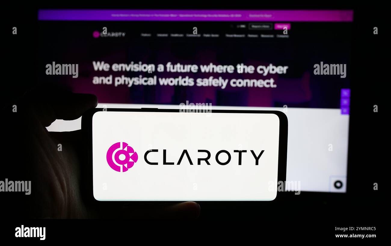 Dans cette illustration photo, une personne tient un téléphone portable avec le logo de la société de cybersécurité Claroty Ltd devant leur page Web d'entreprise. Banque D'Images