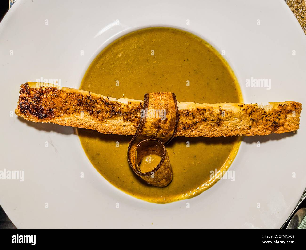 Soupe de bananes cubaine au restaurant Gouverneur de Rouville, Klipstraat, Willemstad, Curaçao – servie avec un grissini de pain grillé et une pelure de banane enroulée en garniture. Le restaurant, situé dans un bâtiment colonial à Otrabanda, allie les traditions culinaires caribéennes et latino-américaines. Banque D'Images