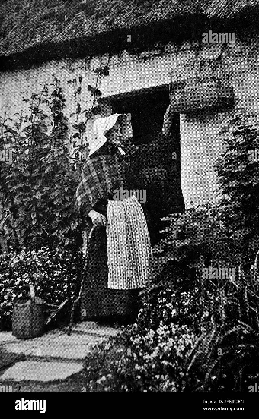 Une dame à la porte d'un chalet au toit de chaume à Swanston, Édimbourg, Écosse, s'occupant d'une cage à oiseaux, c1870. D'après une sélection de photographies sur la vie de l'écrivain victorien Robert Louis Stevenson, publiées par T.N. Foulis en 1912. La qualité de l'image est assez variable - ceux-ci ont été publiés quelque dix-huit ans après le décès de Stevenson. Banque D'Images