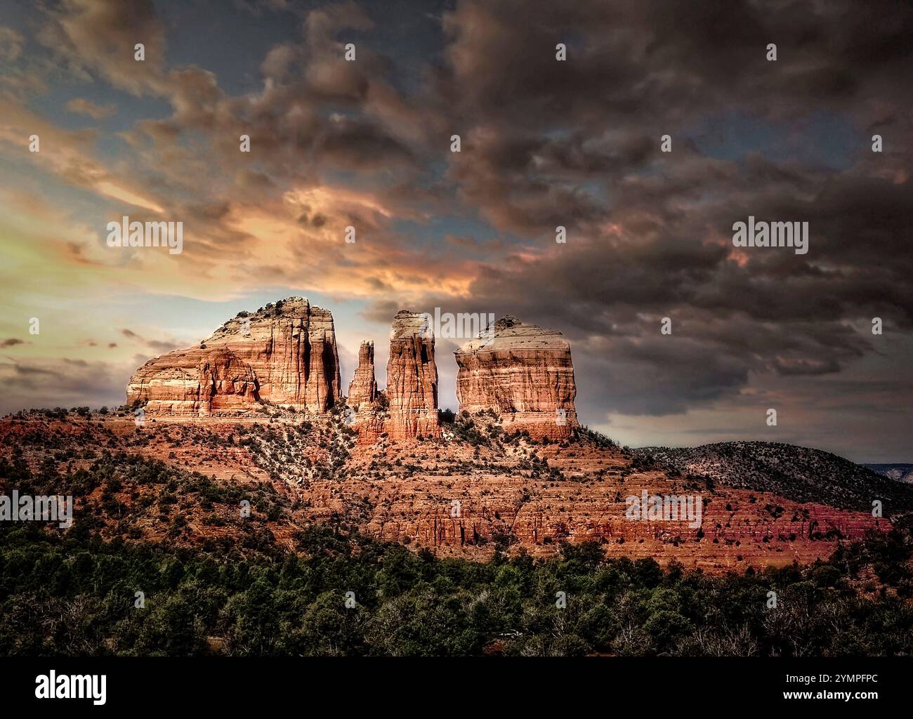 Golden Hour jette une lumière chaude sur les rochers rouges emblématiques de Sedona, avec Cathedral Rock majestueusement debout contre le ciel assombrissant. Banque D'Images