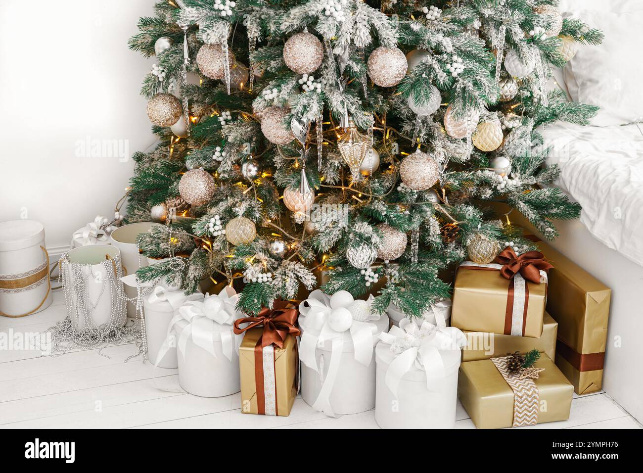 Coffrets cadeaux de vacances enveloppés sous sapin de Noël joliment décoré avec des ornements blancs et dorés. Ambiance joyeuse des vacances d'hiver. Papier peint, Banque D'Images