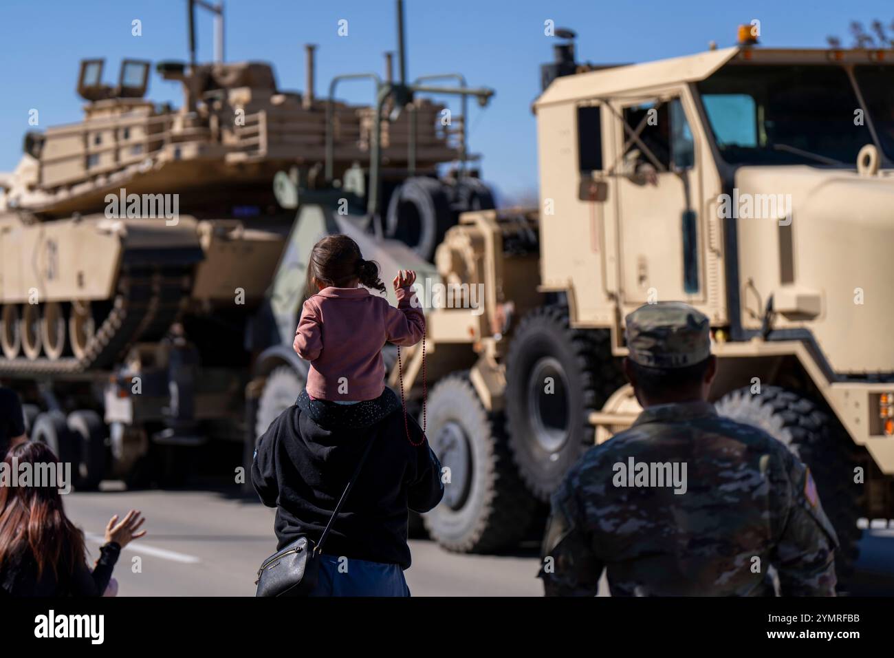 Une enfant sur les épaules de sa mère fait signe devant le chauffeur du transporteur d'équipement lourd M1070A, affecté au bataillon de soutien de la 377e compagnie de transport, 142e division de la brigade de soutien de la division, 1re division blindée, lors de la première parade annuelle de la 337e compagnie de transport à Fort Bliss, Texas, le 20 novembre 2024. Le défilé présente la préparation de l'équipement et les capacités de maintien de l'équipement de la division américaine des chars, assurant ainsi à Old Ironsides d'être prêt à combattre et à gagner quand et où qu'il se trouve. (Photo de l'armée américaine par le SPC Jacob Suess) Banque D'Images