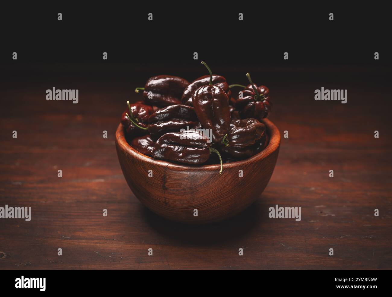 Poivrons habanero au chocolat débordant d'un bol en bois, assis sur une table en bois sombre et rustique Banque D'Images