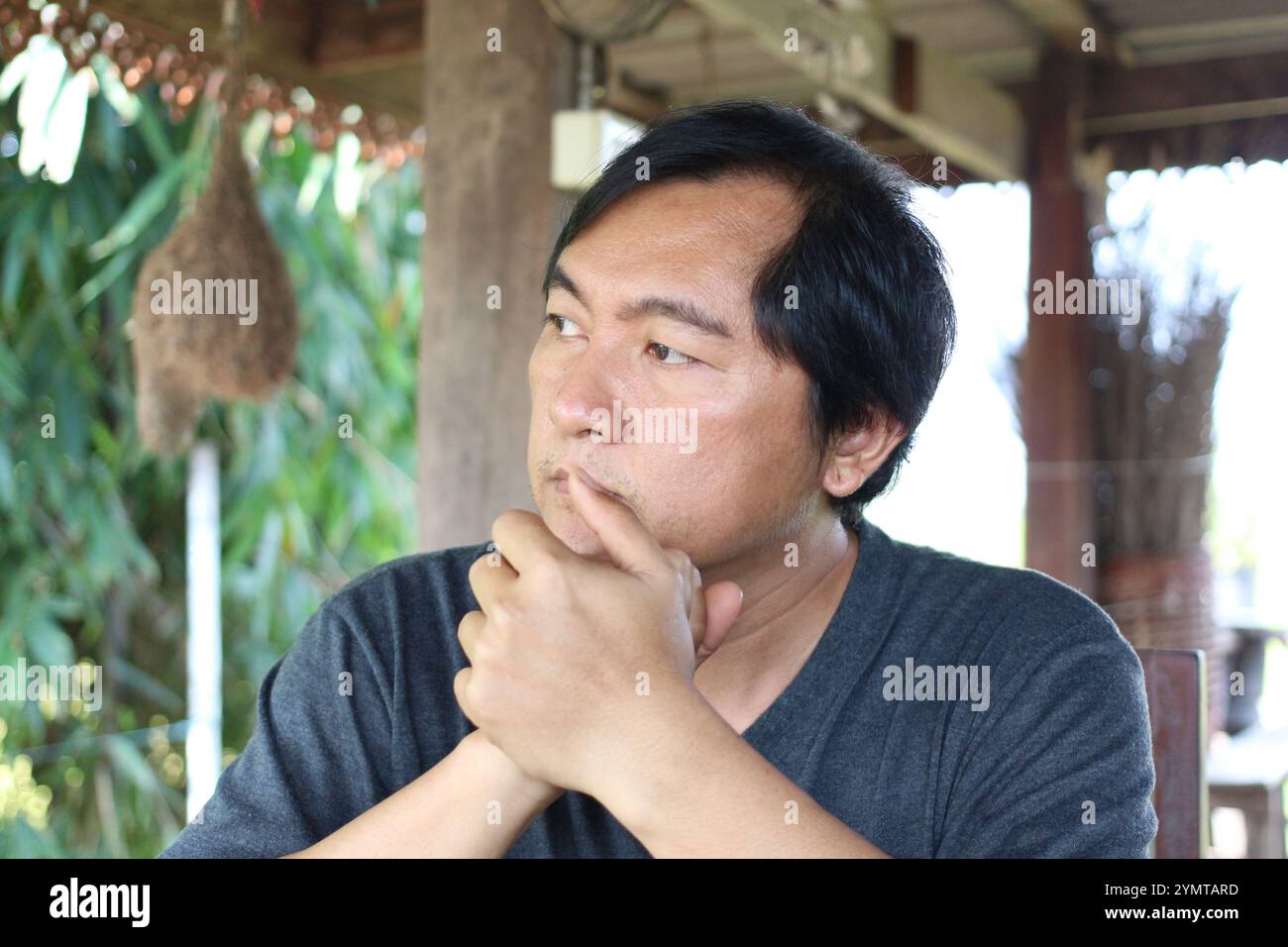 Un homme réfléchi est assis dehors, perdu dans la contemplation profonde. Entouré de verdure naturelle, il exprime un comportement serein qui invite à la réflexion et Banque D'Images