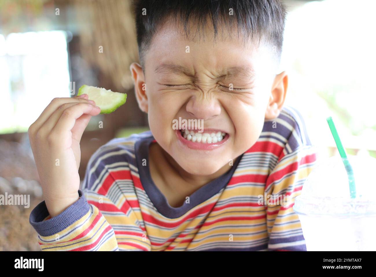 Un enfant joyeux réagit avec joie en dégustant une tranche de citron vert. Le cadre lumineux et coloré met en évidence l'innocence et l'excitation de déguster frais Banque D'Images