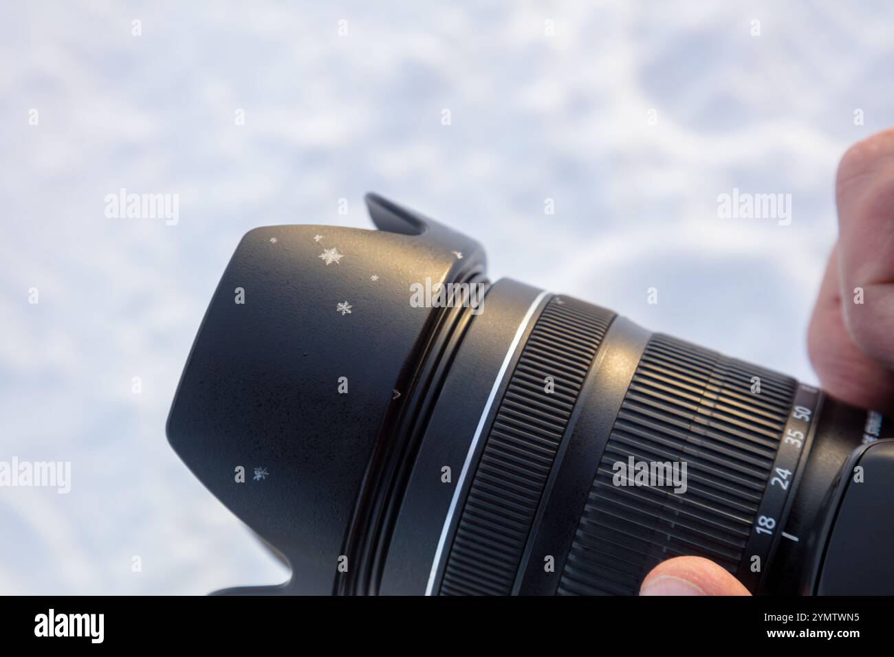 Photographe tenant un appareil photo professionnel sur fond de neige floue. Plusieurs flocons de neige sur la lentille. Gros plan Banque D'Images