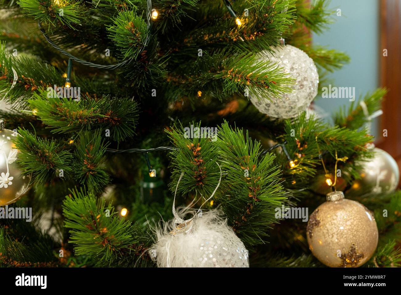 Un arbre de Noël avec de nombreux ornements, y compris une grande boule blanche. Le sapin est illuminé, créant une ambiance chaleureuse et festive Banque D'Images