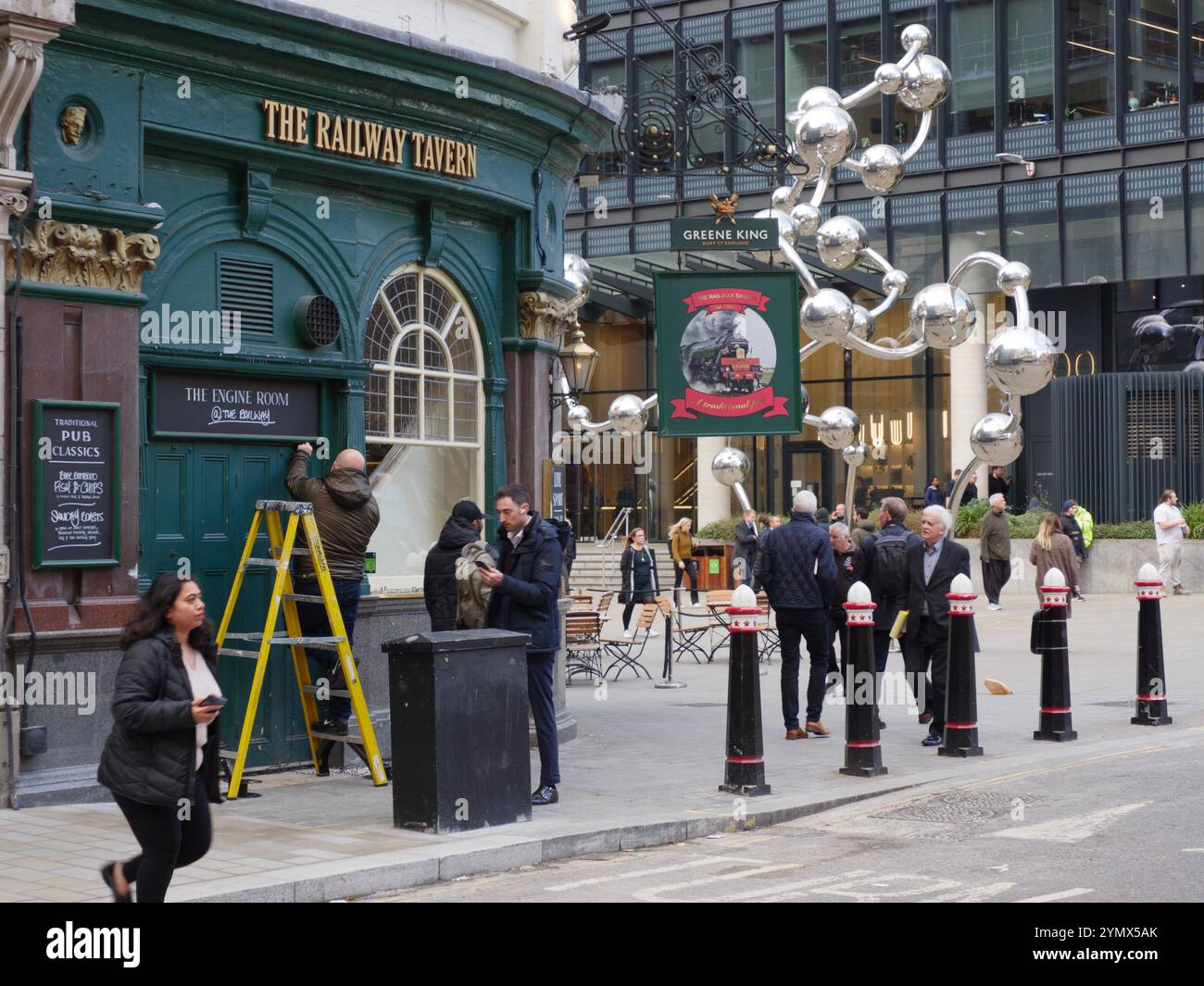 Le pub Railway Tavern exploité par Greene King Liverpool Street, City of London, Royaume-Uni, avec un homme sur échelle réparant les boiseries Banque D'Images