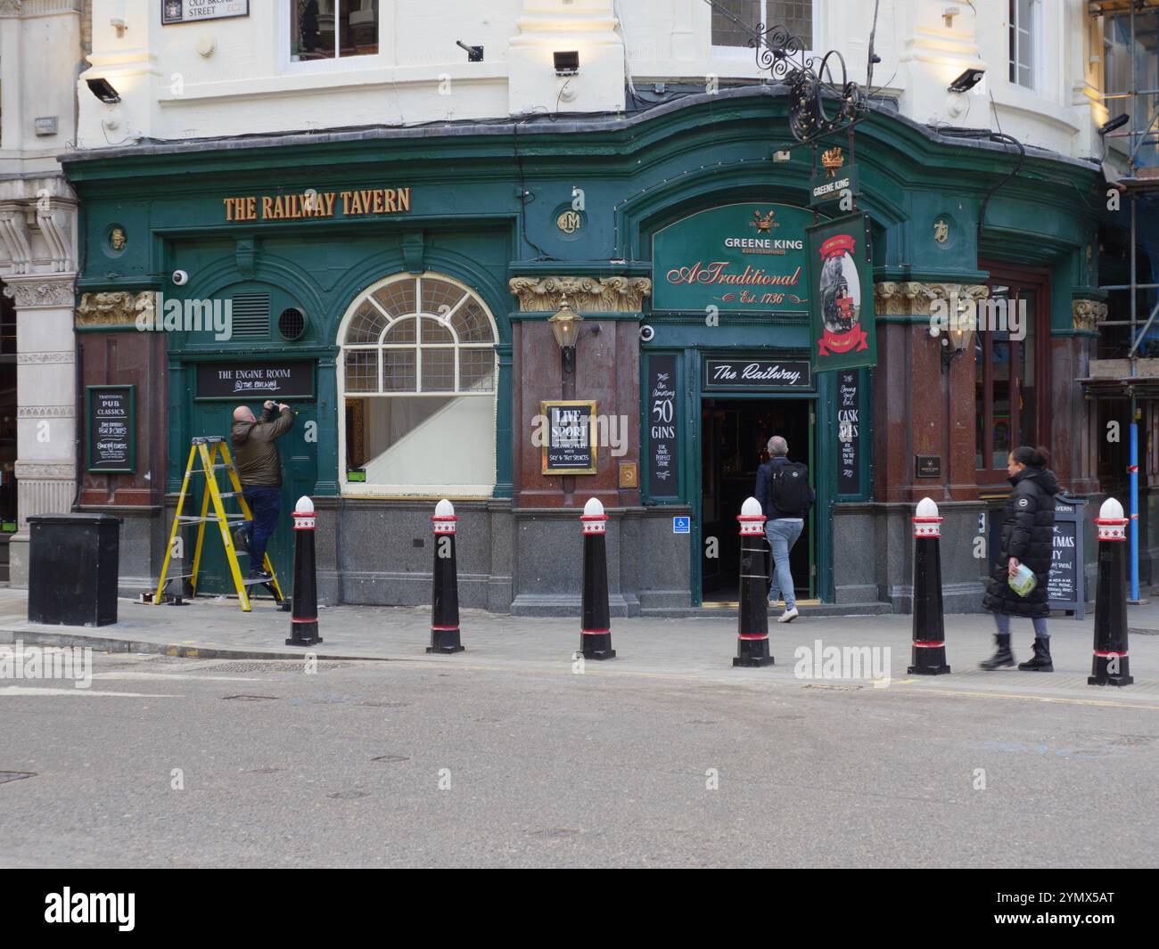 Le pub Railway Tavern exploité par Greene King Liverpool Street, City of London, Royaume-Uni, avec un homme sur échelle réparant les boiseries Banque D'Images