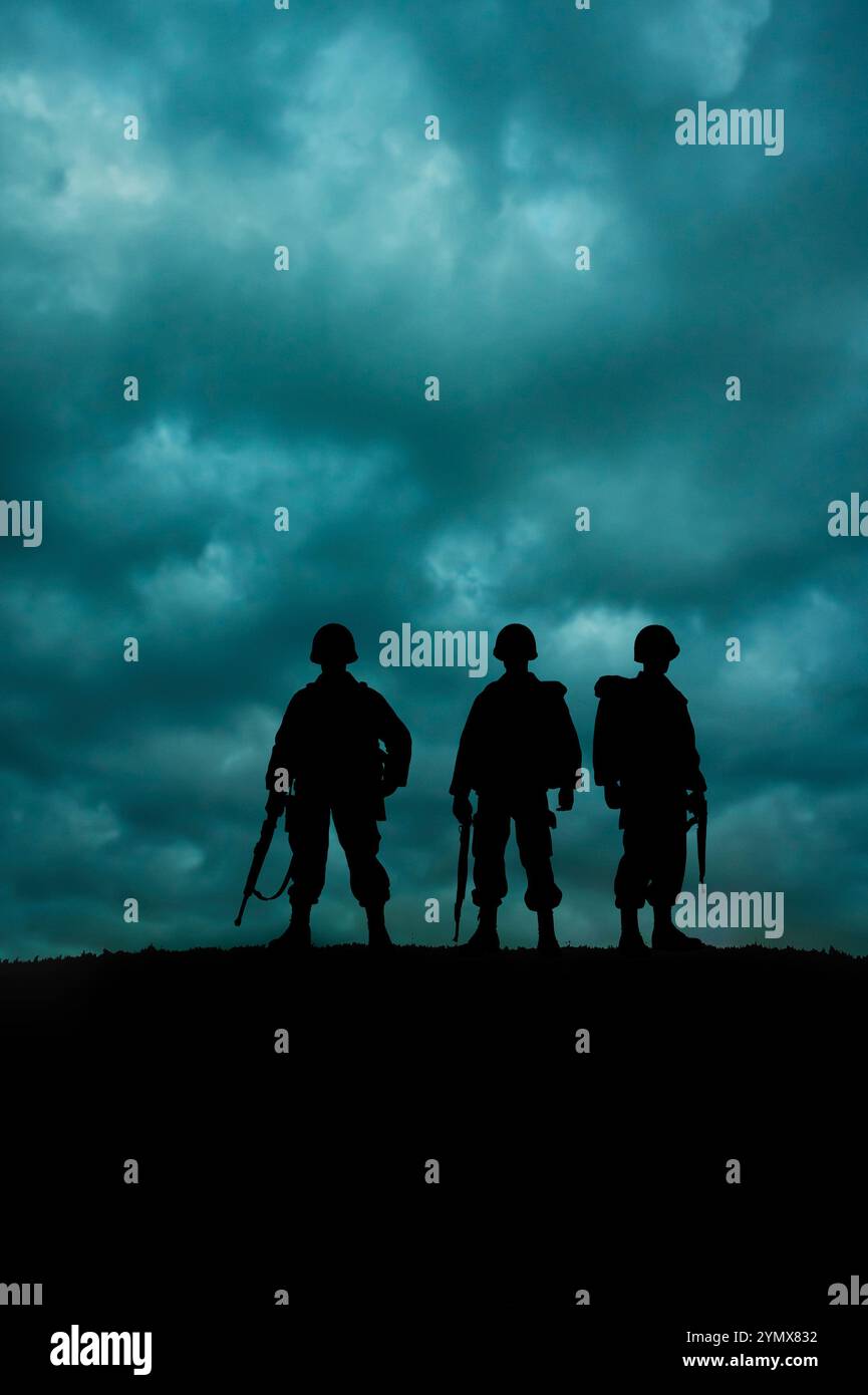 silhouette de trois soldats debout sur une crête avec un ciel nuageux dramatique derrière Banque D'Images