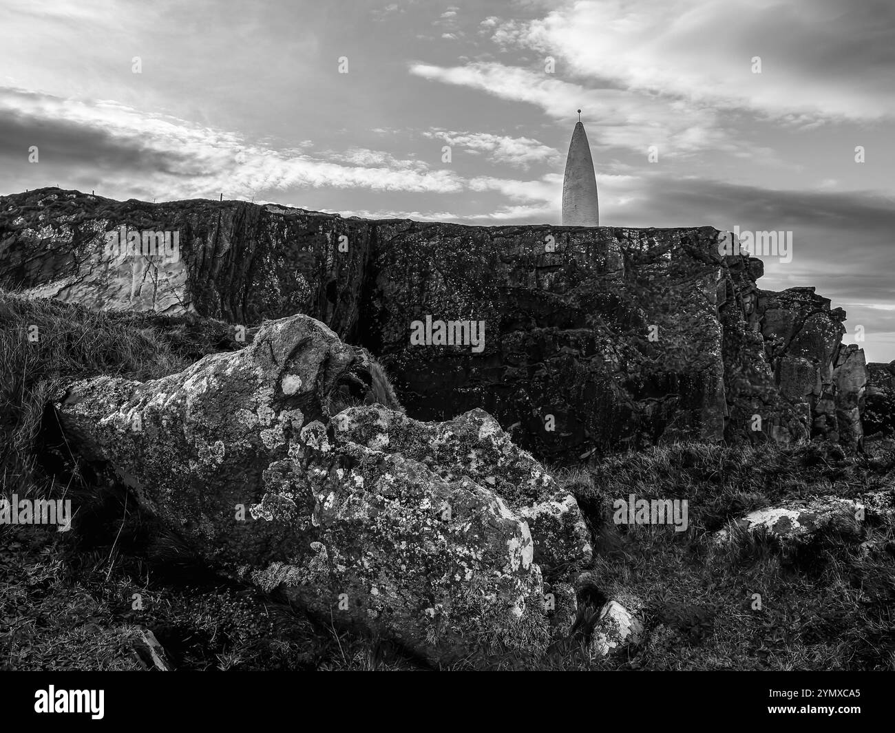 Un affleurement rocheux, partiellement végétalisé, descend vers le haut. Une grande structure blanche et conique est en arrière-plan. Banque D'Images