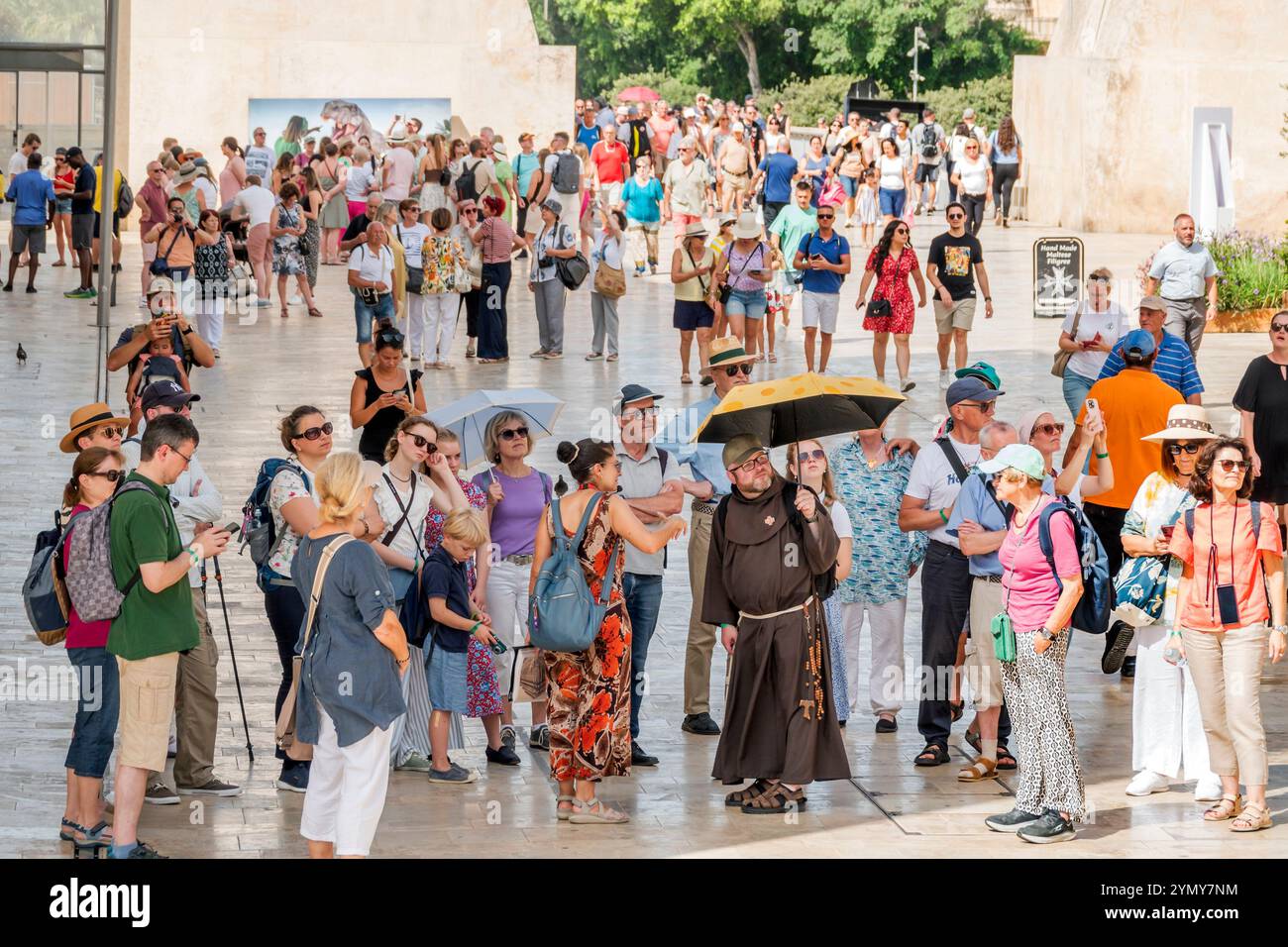 Valletta Malte, Republic Street, guide touristique à pied en groupe, hommes femmes couples familles, moine franciscain moine dirigeant, portant une robe brune, tenant un parapluie, s. Banque D'Images