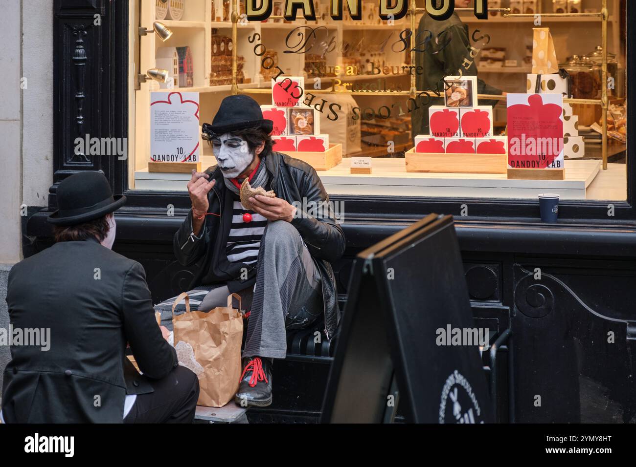 2 artistes mime, artistes de rue mangeant leur déjeuner devant une boutique des Galeries Royales Saint-Hubert, Bruxelles Banque D'Images