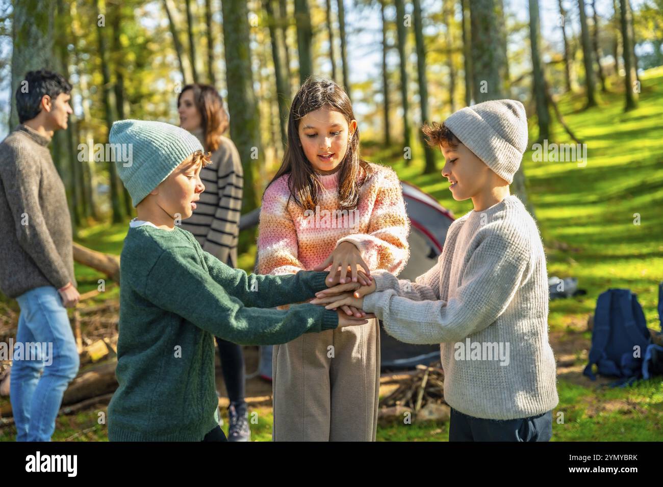 Trois jeunes frères et soeurs caucasiens jouant en profitant du camping dans la forêt avec leurs parents Banque D'Images