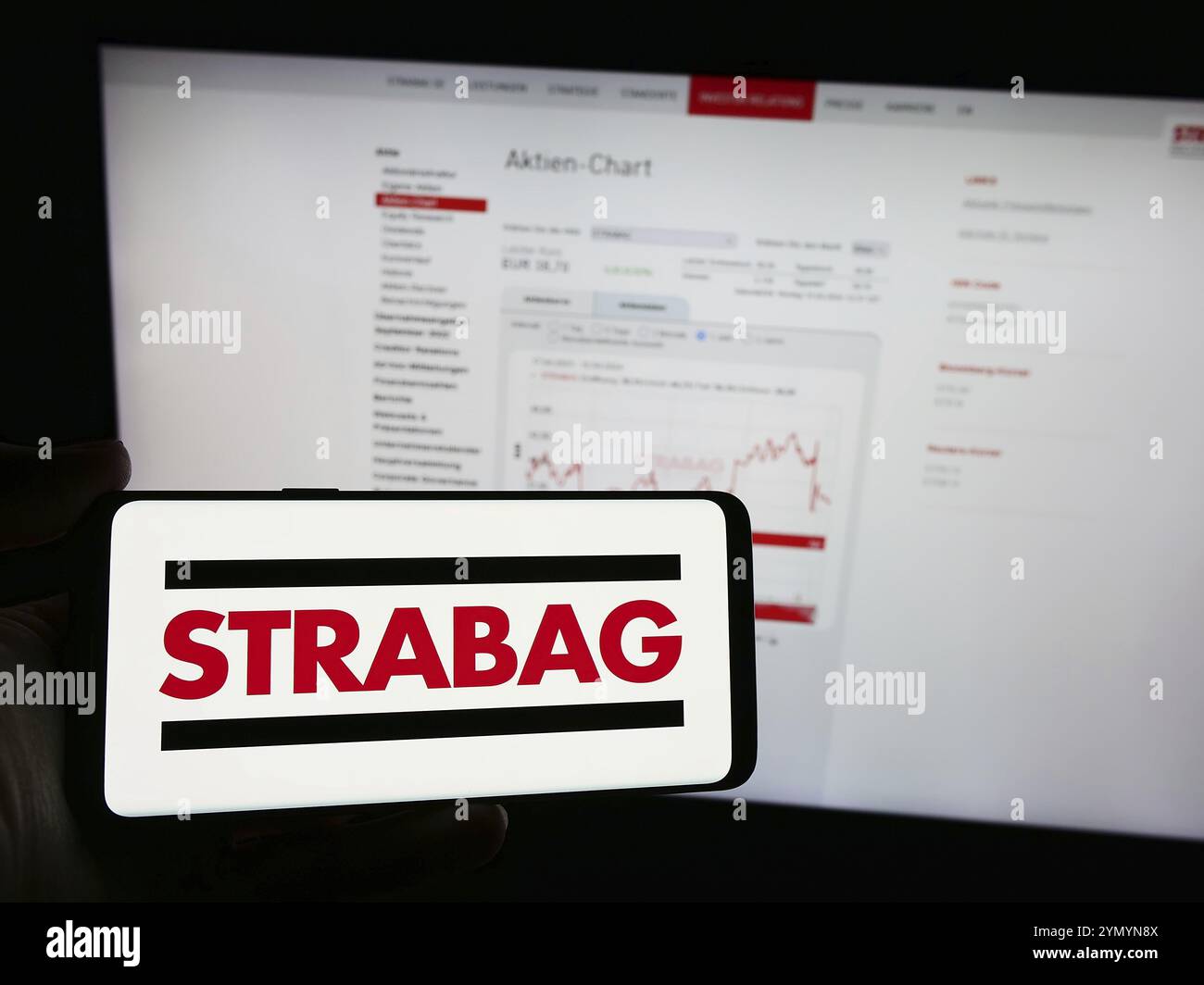 Stuttgart, Allemagne, 04-15-2024 : personne tenant un téléphone portable avec le logo de l'entreprise de construction autrichienne Strabag se en face de la page Web de l'entreprise. Mise au point Banque D'Images