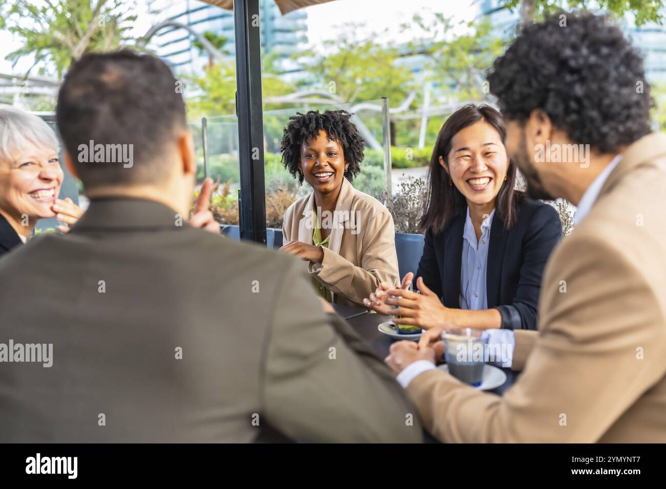 Des femmes d'affaires souriantes parlant avec des collègues multiethniques assis à boire du café dans une cafétéria Banque D'Images