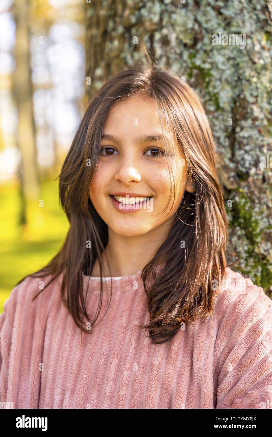 Gros plan portrait vertical d'une fille souriante caucasienne avec des vêtements roses appréciant la nature appuyée sur l'arbre Banque D'Images