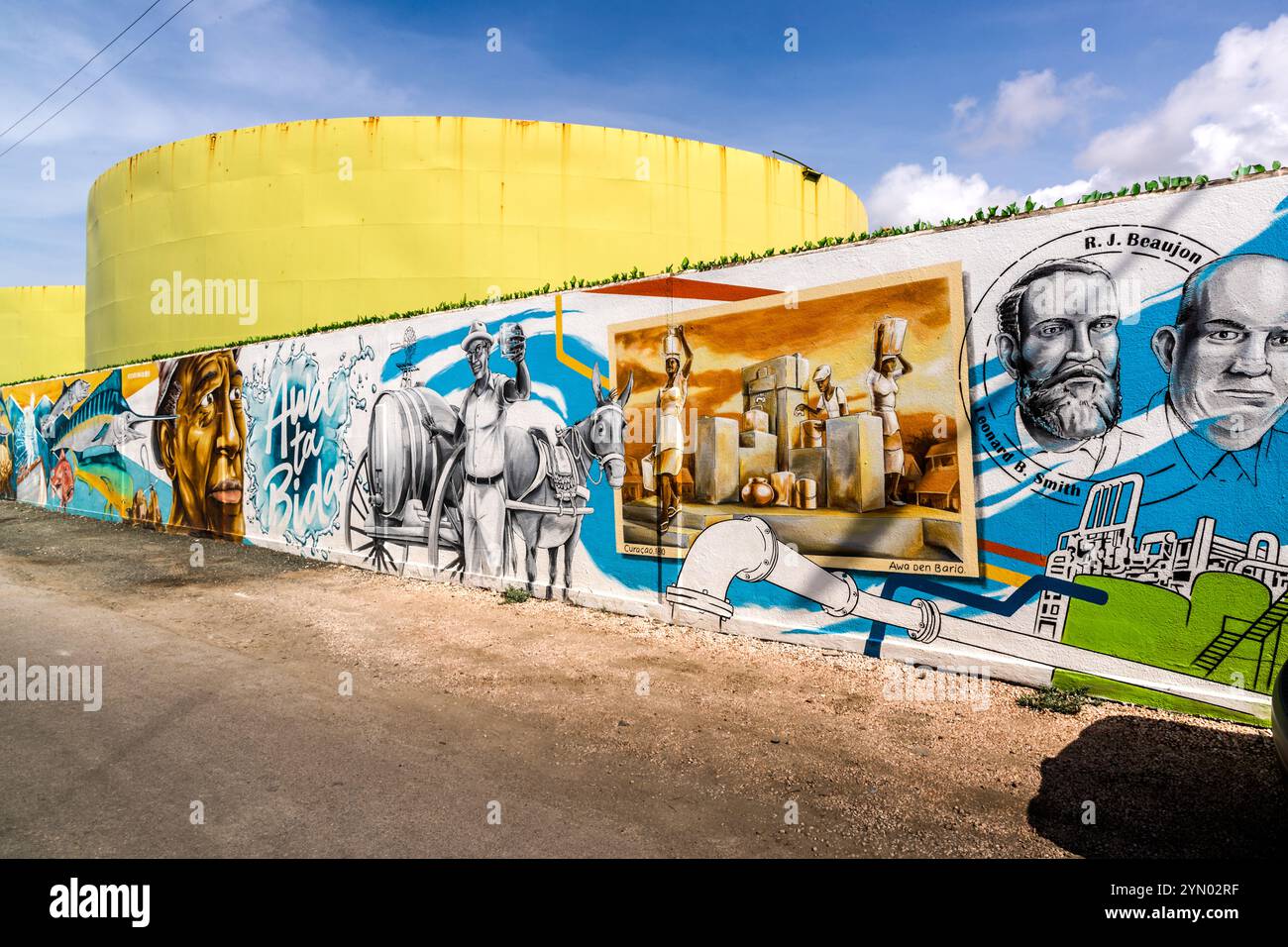 La fresque "Awa ta Bida" (Papiamentu pour "L'eau est la vie") par Sander van Beusekom (BLEND) recouvre le mur extérieur de l'ancienne usine de désalinisation d'eau de mer Aqualectra, Willemstad, Curaçao. Elle raconte l'histoire de l'approvisionnement en eau potable de l'île : des porteurs d'eau historiques, des portraits de personnalités telles que R.J. Beaujon, et l'inscription "Awa ta Bida". La désalinisation de l'eau de mer a commencé à Curaçao en 1928. John F. Kennedy Boulevard, Willemstad. Banque D'Images
